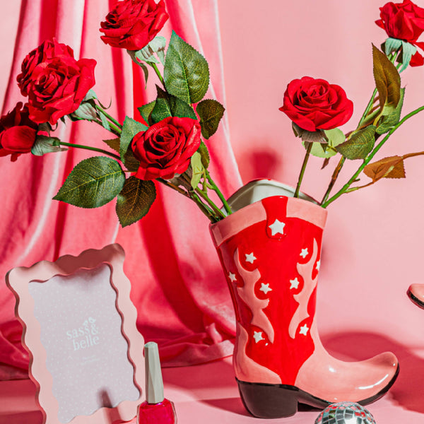 Florero bota western con rosas en decoración femenina estilo pop chic sobre fondo rosa