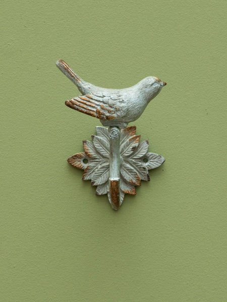 Perchero rústico de hierro fundido con forma de pájaro sobre hojas