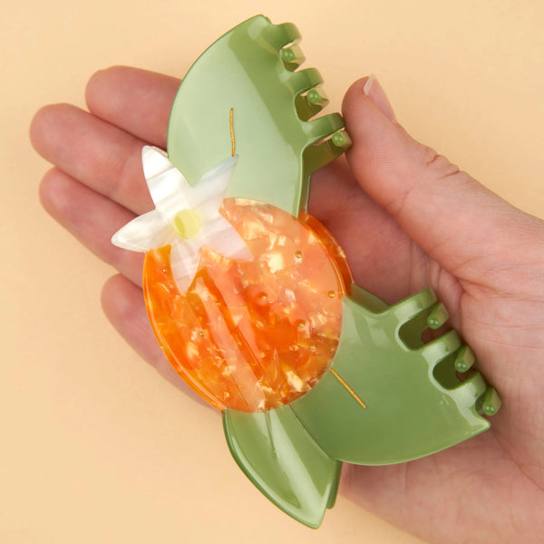 Mano sujetando pinza Coucou Suzette flor de naranjo para mostrar tamaño y diseño.