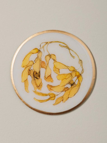 Posavasos de metal con ilustración de semillas amarillas y borde dorado estilo botánico artístico