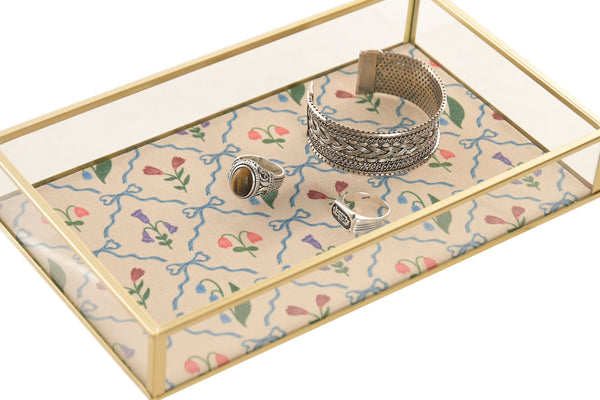 Bandeja organizadora de cristal con joyas y estructura de latón dorado.