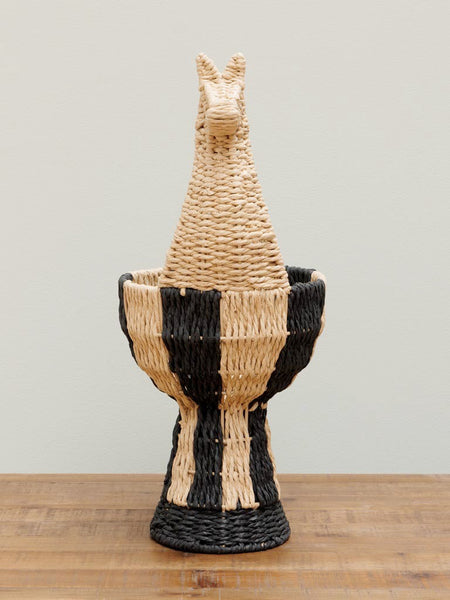 Panera de fibras naturales con forma de llama vista frontal sobre superficie de madera