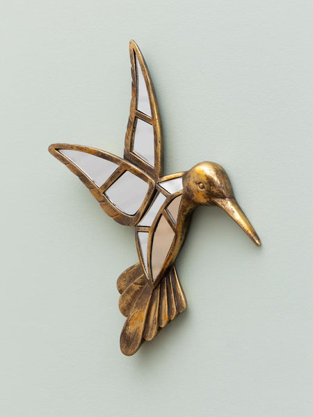 Adorno de pared con forma de colibrí dorado y espejos sobre pared verde clara