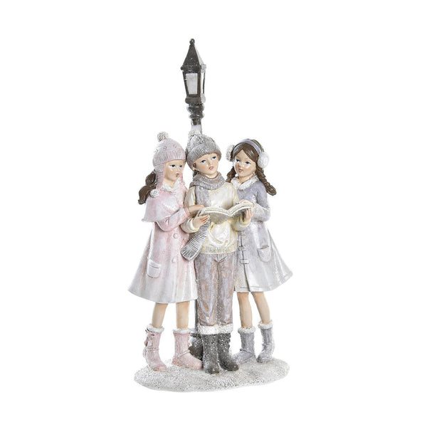 Figura navideña de niñas cantando villancicos bajo farola