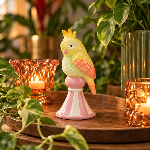 Figurita Loro Amarillo de cerámica integrada en una composición decorativa con plantas y velas.