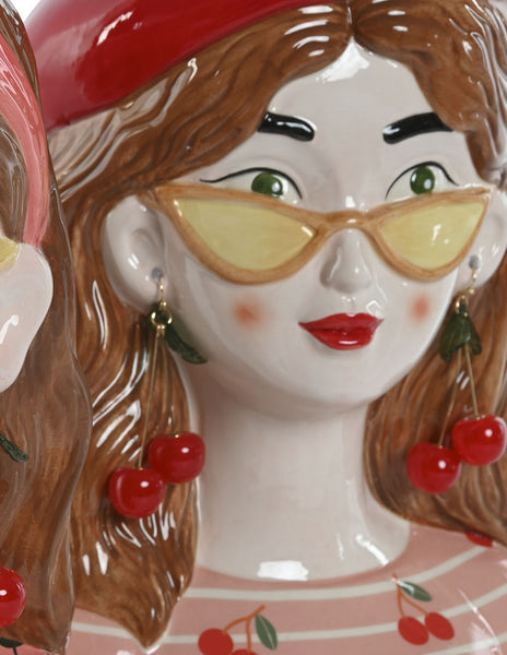 Primer plano jarrón cerámico con pendientes de cerezas y gafas amarillas – decoración femenina y divertida.