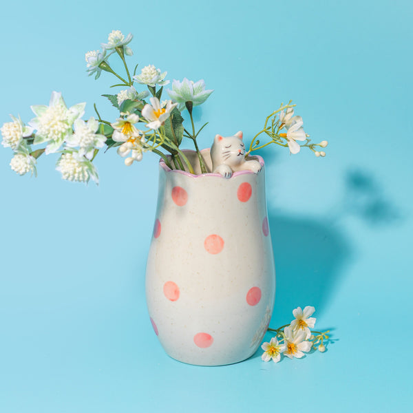 Jarrón decorativo con gatito y arreglo de flores blancas.