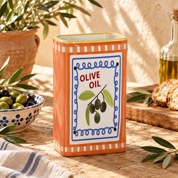 Jarrón Lata de Aceite Naranja decorando una cocina mediterránea junto a aceitunas y ramas de olivo.