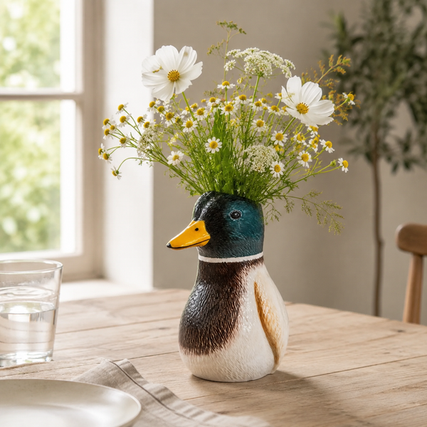 Jarrón pato de cerámica con flores blancas sobre una mesa de madera