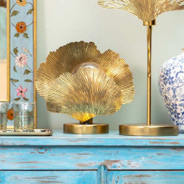 lámpara escultórica dorada sobre mesa de madera decapada