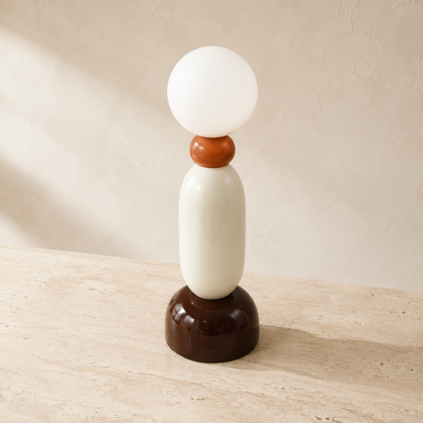 Lámpara decorativa de mesa en tonos marrón, crema y naranja sobre consola clara