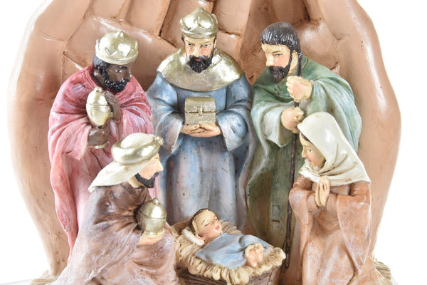 belén navideño con manos rezando y figuras del pesebre