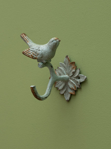 Gancho decorativo de hierro fundido con pájaro en acabado envejecido, fijado a pared verde