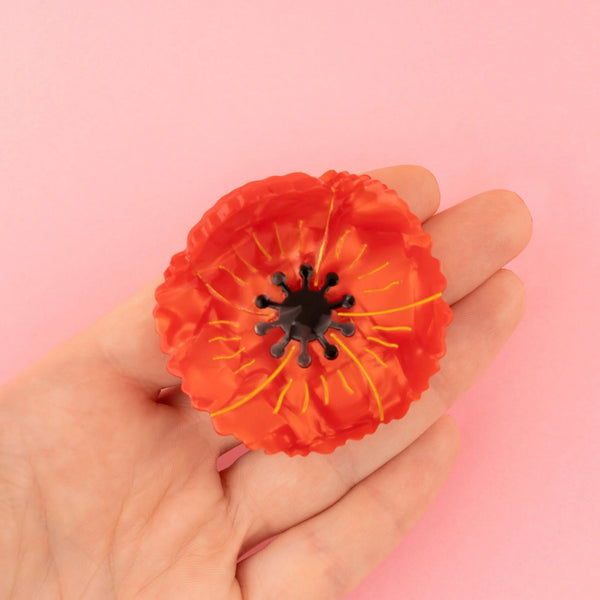 Pinza Amapola Coucou Suzette de 5 x 5 cm mostrada sobre una mano para apreciar su tamaño.