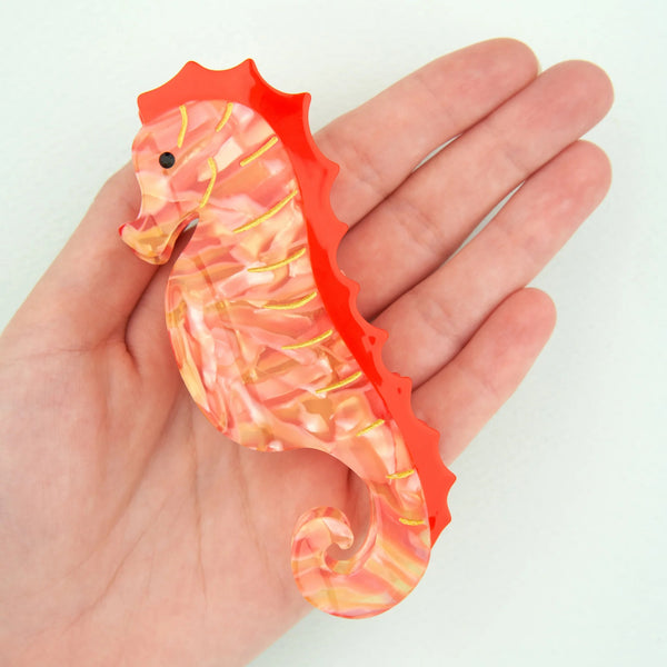 Pinza Caballito de Mar Coucou Suzette de 4 x 10 cm mostrada sobre una mano para apreciar su tamaño.