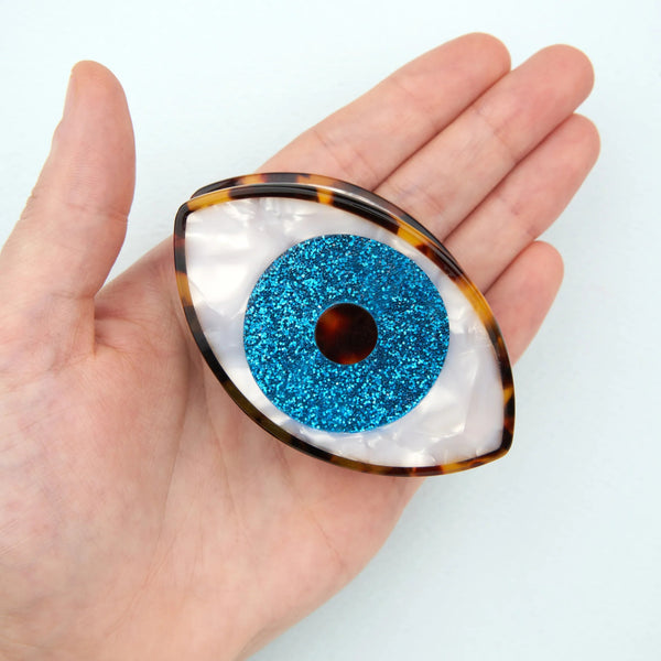 Pinza de pelo con forma de ojo azul Coucou Suzette mostrada sobre una mano para apreciar su tamaño.