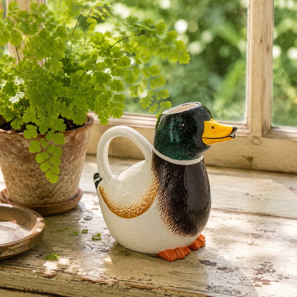 Regadera pato de cerámica decorando un rincón junto a una planta verde