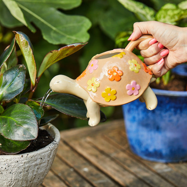Persona utilizando regadera de tortuga de cerámica para regar plantas, accesorio decorativo funcional y colorido