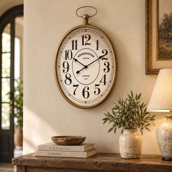Reloj de pared Kensington Station ovalado en ambiente clásico con muebles de madera y decoración vintage.